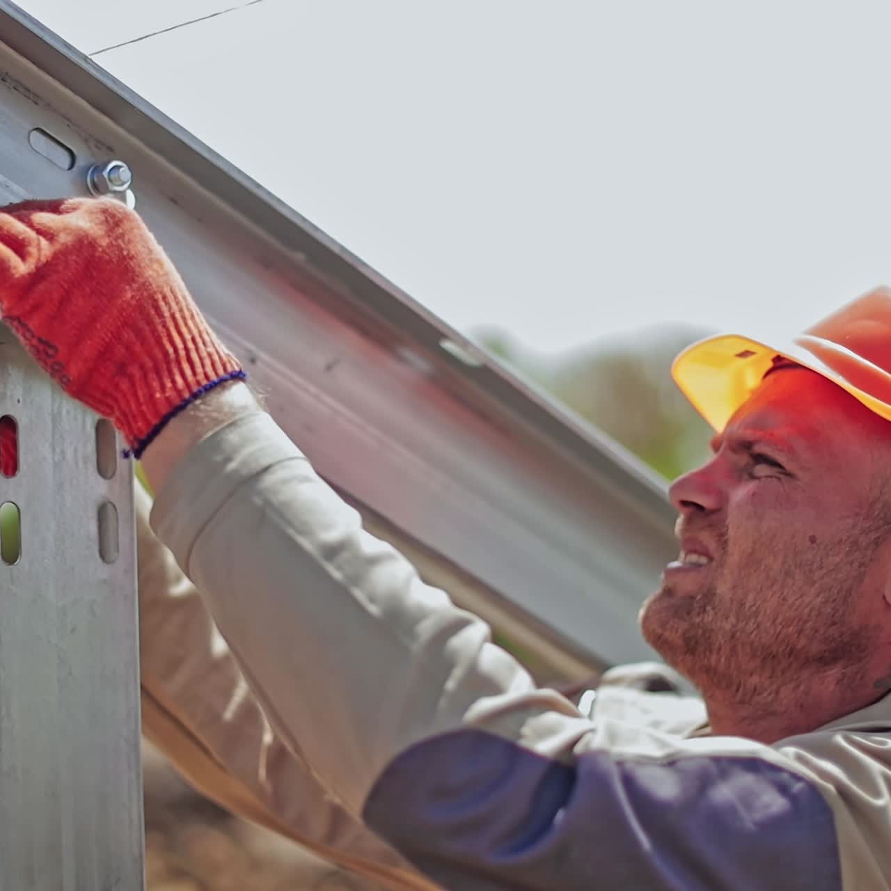 Worker in a uniform and hard hat attaching metal base. Engineer installing metal basis for photovoltaic panel on a solar farm.