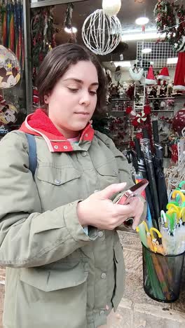 a woman is looking at her phone while standing in front of a christmas ornaments.