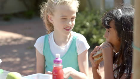 caucasian girl shares a meal with a biracial girl outdoors at school