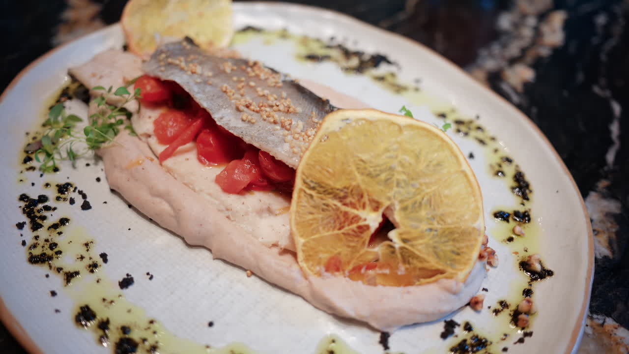 Close up of a beautifully plated fish fillet with sauce, lemon slice, and herbs