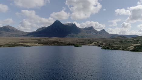 aerial travelling low above a loch with the prominent mountain range of ben loyal in the background