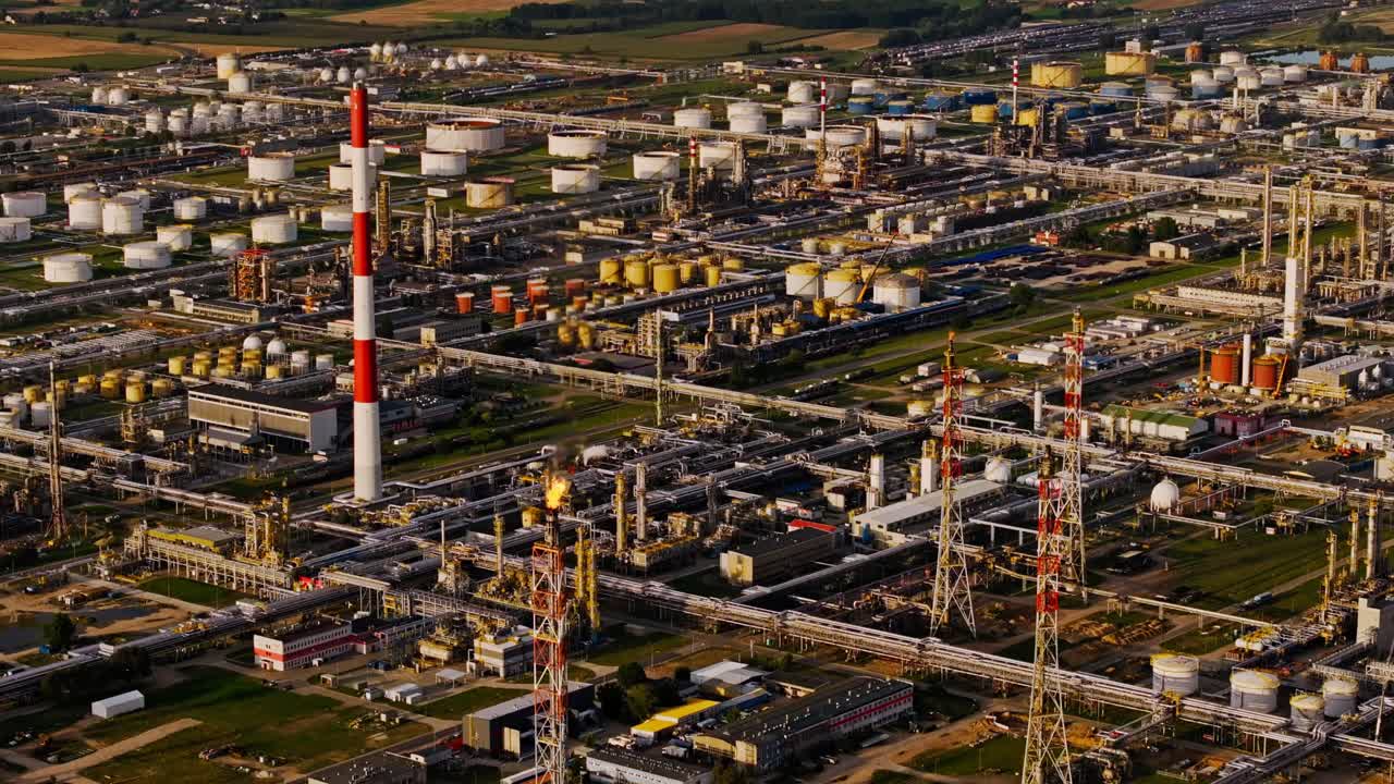 Industrial refinery complex with fuel tanks and striped smokestack under sunset