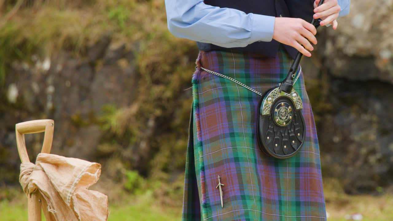 Traditional musician in tartan kilt prepares bagpipes at outdoor Highland Games, natural daylight