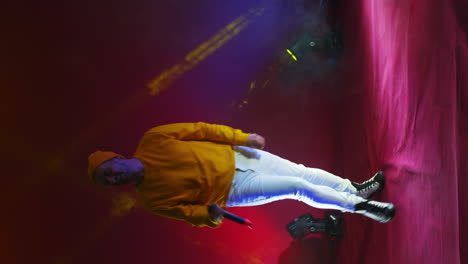 video vertical. un cantante con un traje amarillo baila y canta con un micrófono de color neón. salta y mueve vigorosamente.