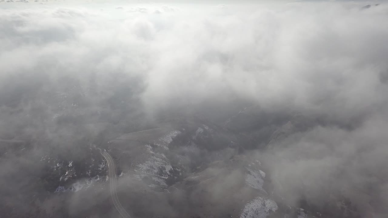 An aerial view of a snowy mountain pass while flying through hazy clouds