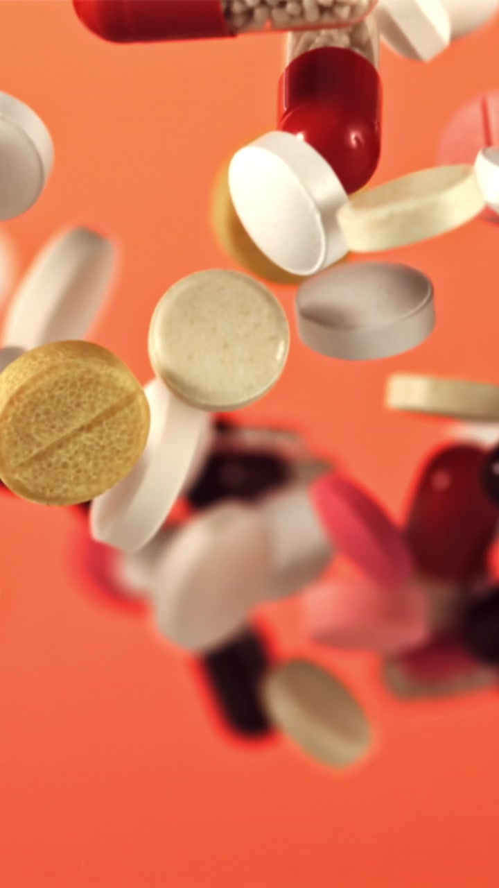 Movimento rallentato di pillole e capsule colorate che galleggiano su uno sfondo arancione