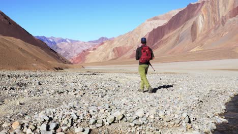 hiker jumping across a river in the andes mountains during a trekking in mendoza, argentina.