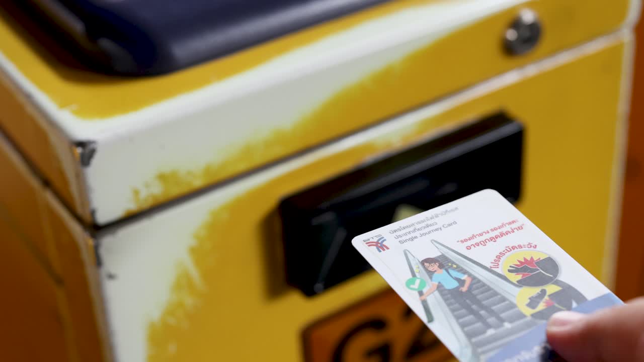 Close-up hand inserting safety-notice transit card into worn yellow ticket machine, shallow focus