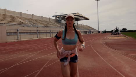 female runner listening to music and running on stadium track