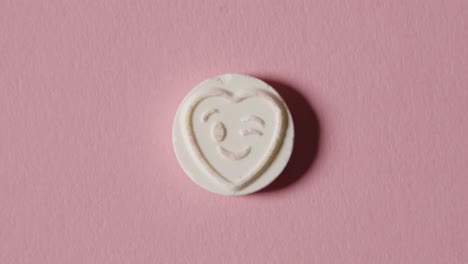 heart candy with winking emoji on pink background