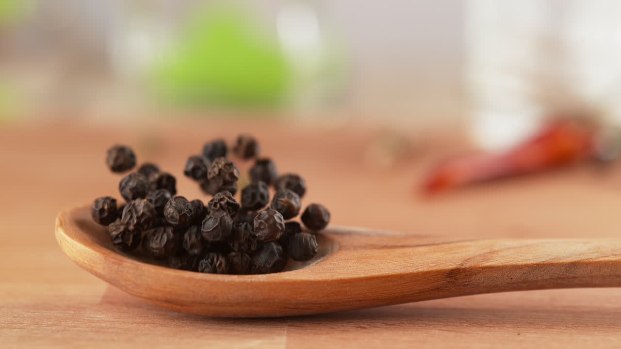 granos de pimienta negra en cuchara de madera caen sobre la mesa, rebotan y se dispersan en cámara lenta y macro