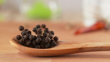 black peppercorns on wooden spoon fall onto the table, bounce and scatter in slow motion and macro