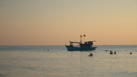 puesta de sol en la playa con un barco de pesca y personas nadando