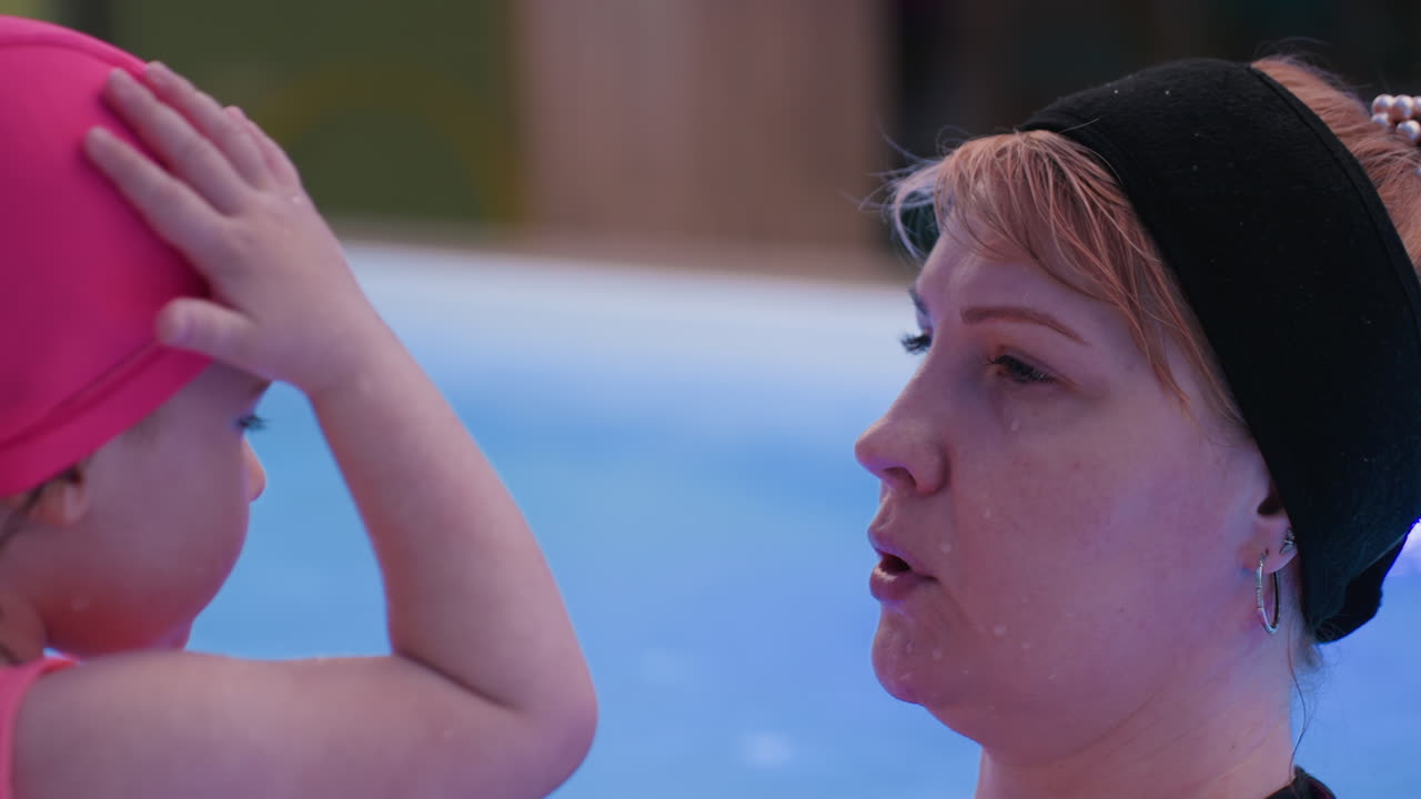Swim coach gently dressing little child's head pant near poolside, focusing on preparation for water activity, tender moment highlighting care, innocence, and learning in safe aquatic environment