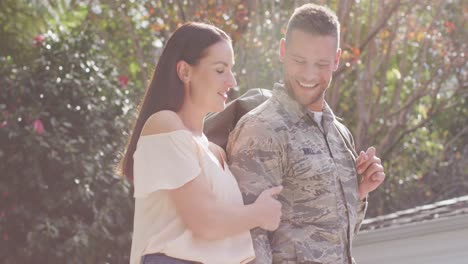 happy caucasian male soldier carrying bag walking with his smiling wife in garden