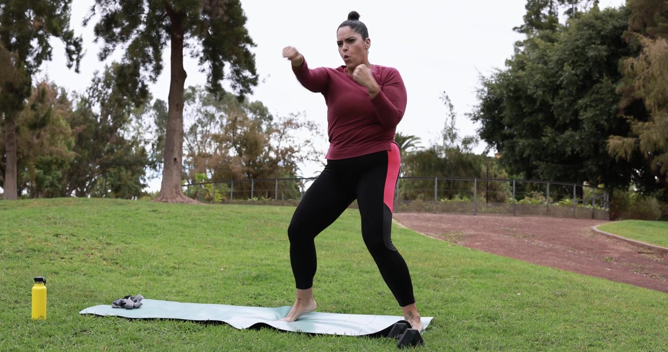 Kvinde der øver bokseslag på yogamåtte i park