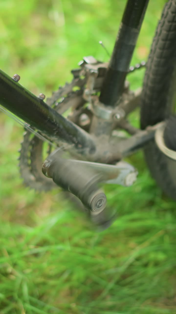 primer plano de un individuo con zapatillas grises tocando y girando el pedal de una bicicleta estacionada en un campo de hierba mientras toca su tobillo, el pie permanece en el pedal mientras la bicicleta se ajusta