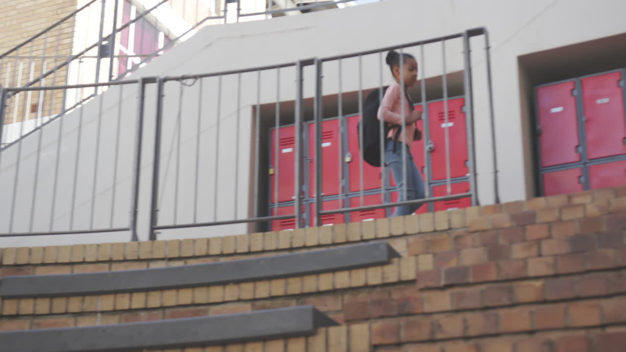 Walking down stairs, African American girl with backpack heading to school lockers
