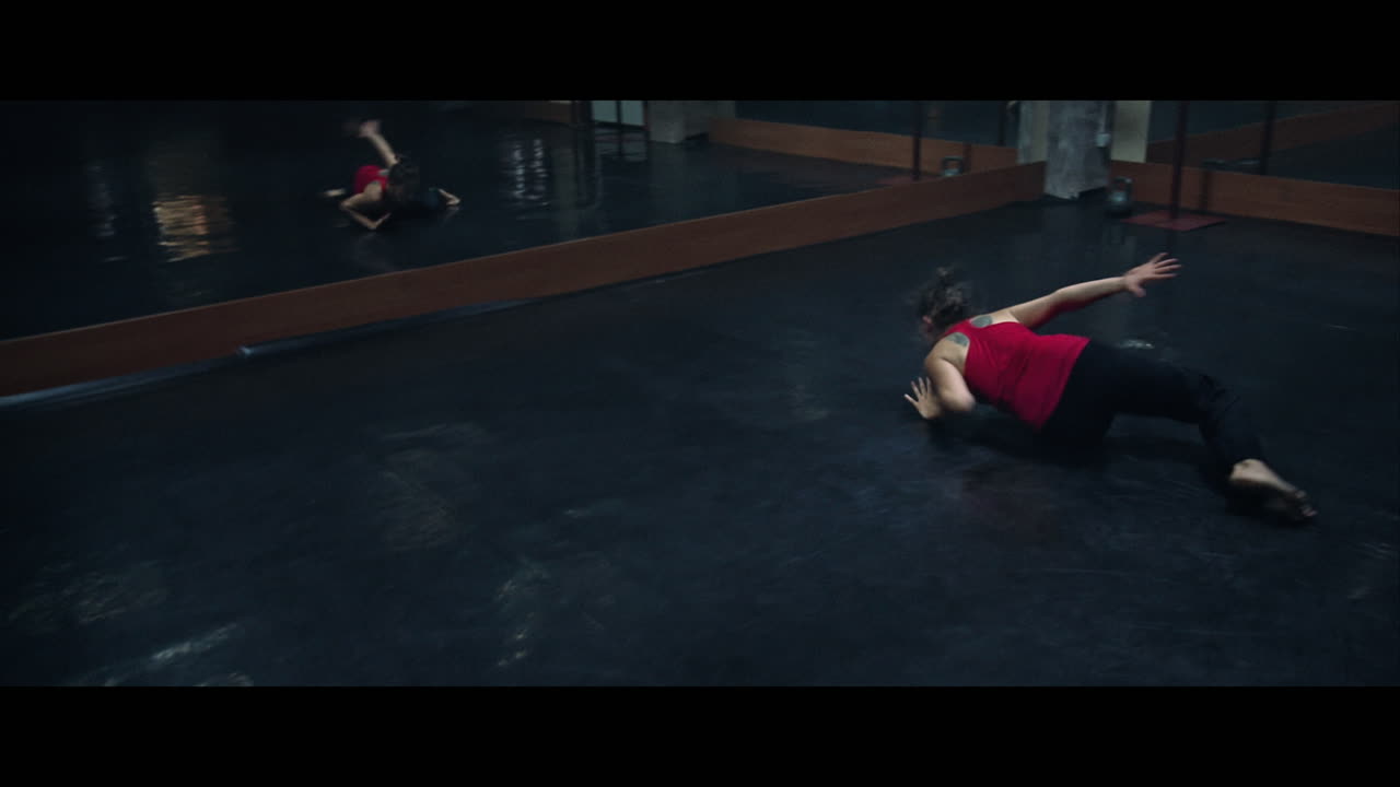 A young woman practices modern dancing and ballet in a moody room full of mirrors