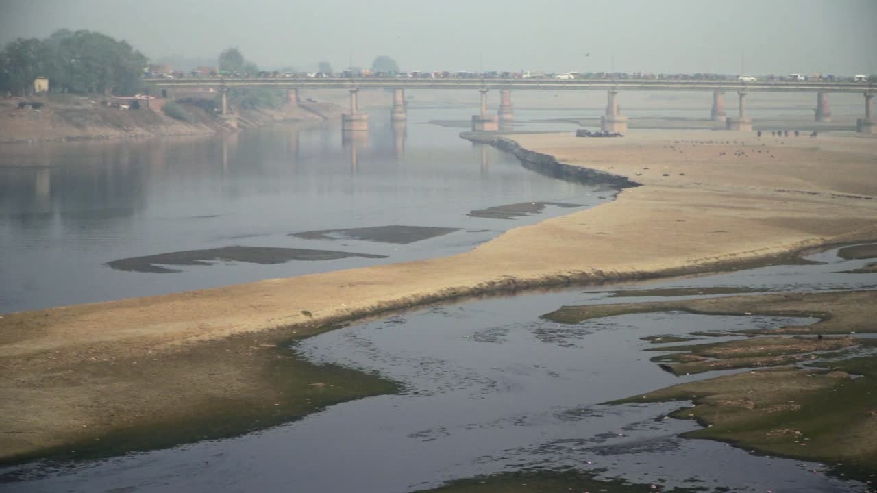 pan rápido al río vacío con su agua estancada, y un puente, con tráfico, árboles, torre eléctrica y casas con el río