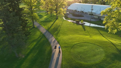 golfers walk on path at golf course. pretty spring day. american leisurely activity. aerial view during sunset at golden hour.