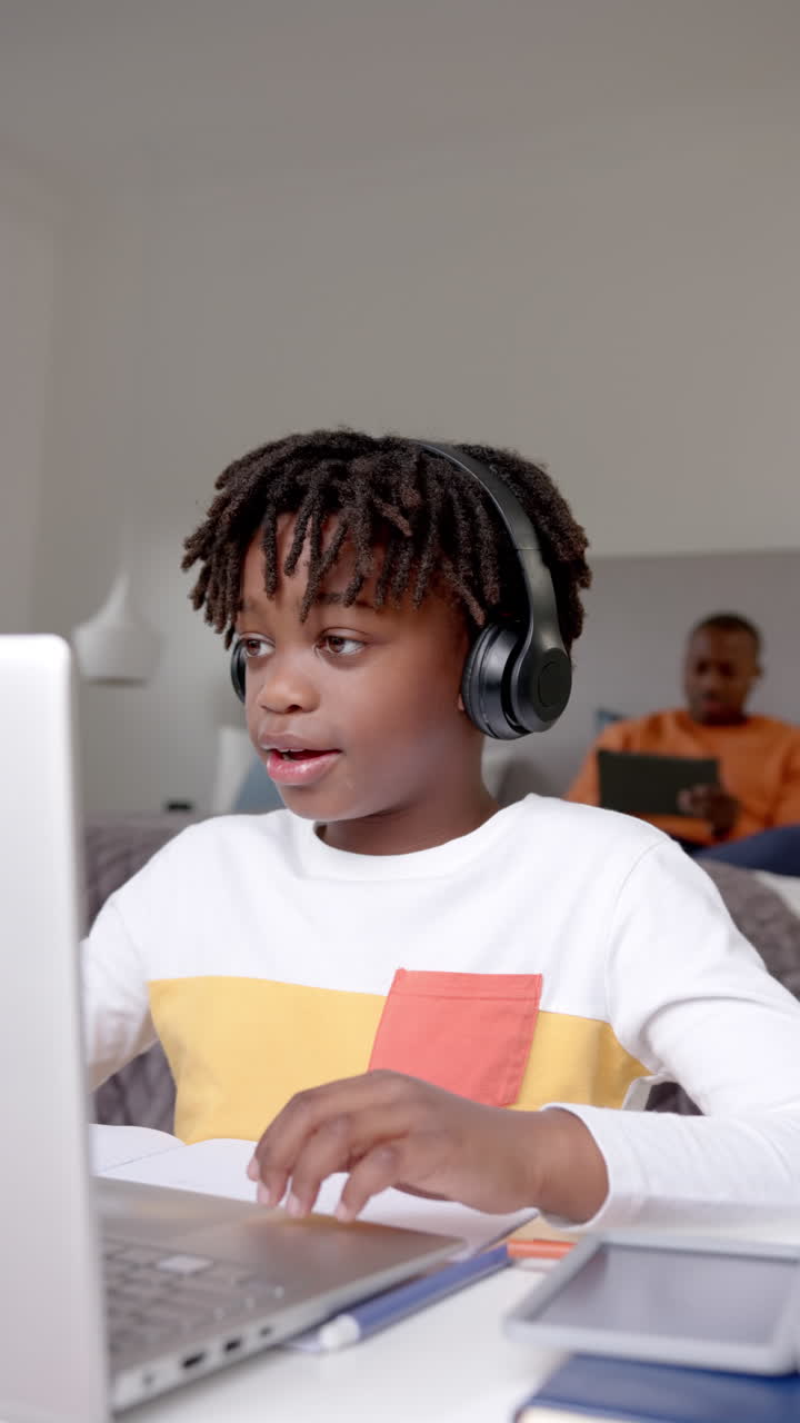 Vertical video of african american boy using laptop for online lesson at home, slow motion