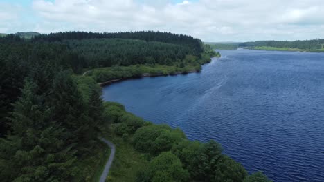 Idyllic-blue-water-reservoir-lake-woodland-hiking-walk-aerial-view-descending-to-shoreline