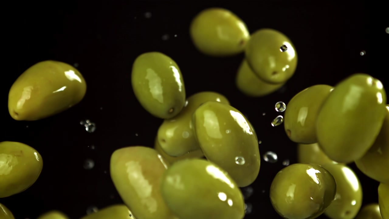 Olive verdi fresche in caduta con schizzi d'acqua su sfondo nero