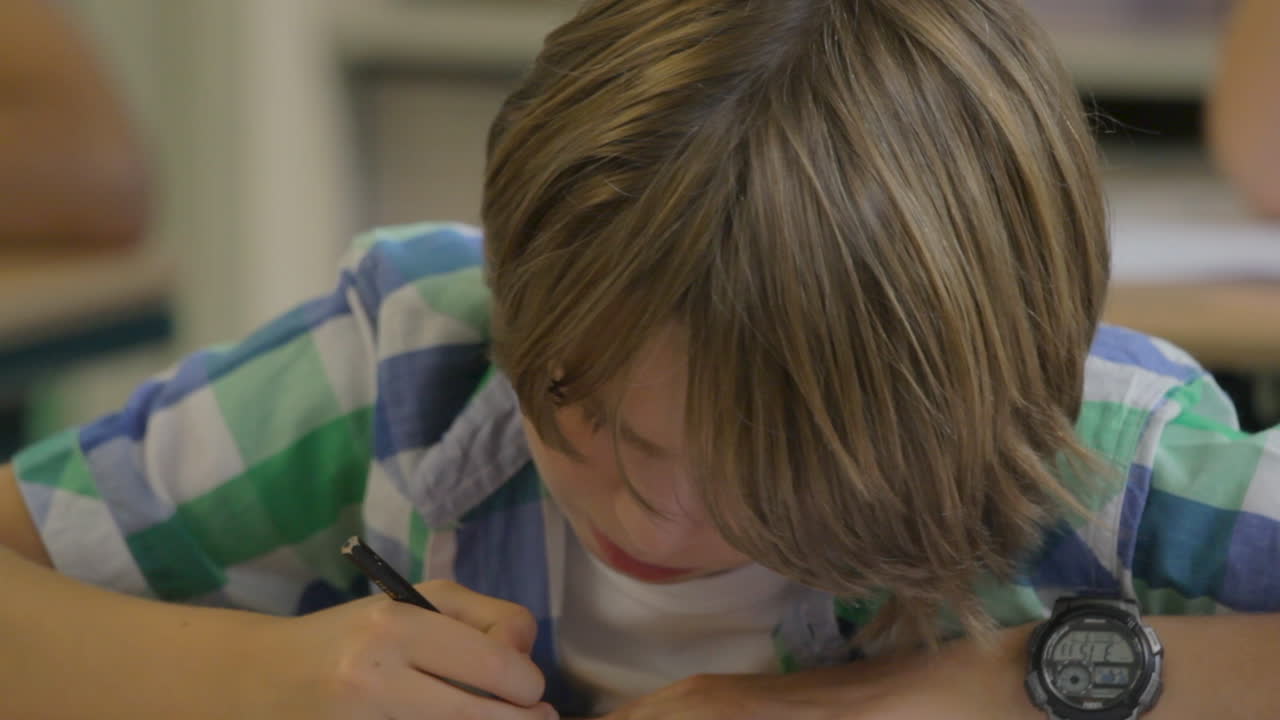 Un giovane ragazzo che disegna in classe e alza lo sguardo quando viene chiamato dall'insegnante.