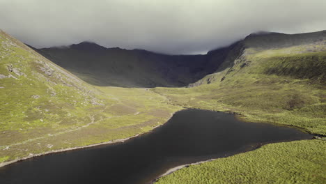 hermosa antena de un pequeño río con un lago dentro de montañas cubiertas de hierba con una cordillera cubierta de nubes pedregosas que se encuentra detrás-1