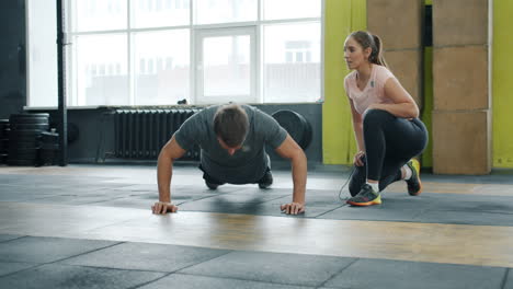 man doing push-ups with a fitness trainer in a gym