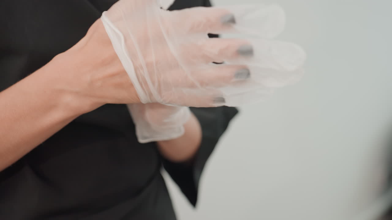 Parrucchiere che indossa i guanti prima del servizio, uniforme nera, primo piano delle mani e dei guanti in lattice, preparazione accurata per la colorazione dei capelli, attenzione all'igiene e alla sicurezza, manicure curata e dita composte, calma