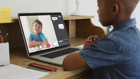 african american boy holding a pencil having a video call on laptop at home
