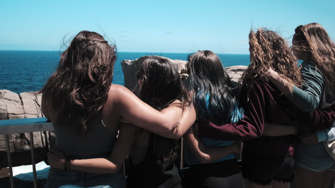 Girls hugging and looking down at the Gap lookout, near Watsons Bay. on the Coast of Sydney, on a sunny day, in Australia - tracking, pan shot