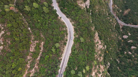 un cautivo avión no tripulado disparado de arriba hacia abajo siguiendo hábilmente un coche a lo largo de una sinuosa carretera de montaña