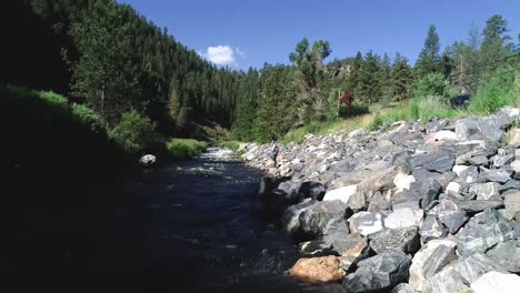 a fly fisherman casts along the banks of a high mountain river