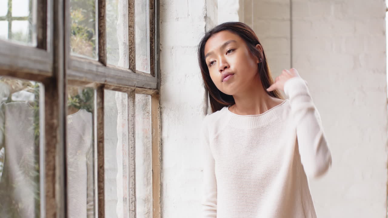 Gazing out window, asian young woman reflecting quietly in living room, at home