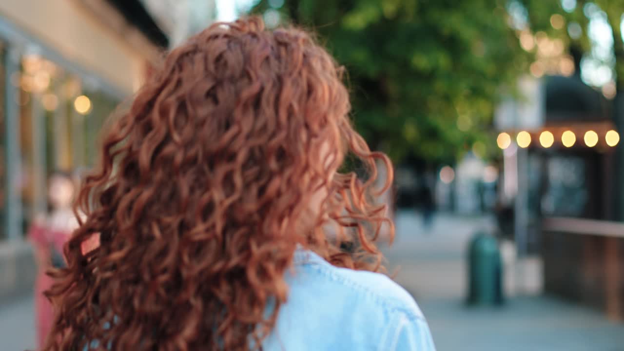 길을 걸어가는 빨간 머리 여자의 뒷모습, 그리고 나서 그녀는 돌아서서 카메라를 쳐다본다