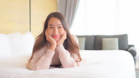 A-young,-very-cute-woman-lying-on-a-comfortable-hotel-suite-bed-has-her-chin-propped-up-in-her-hands-and-smiles