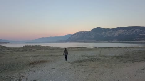 Forward-drone-shot-of-a-girl-walking-towards-a-lake