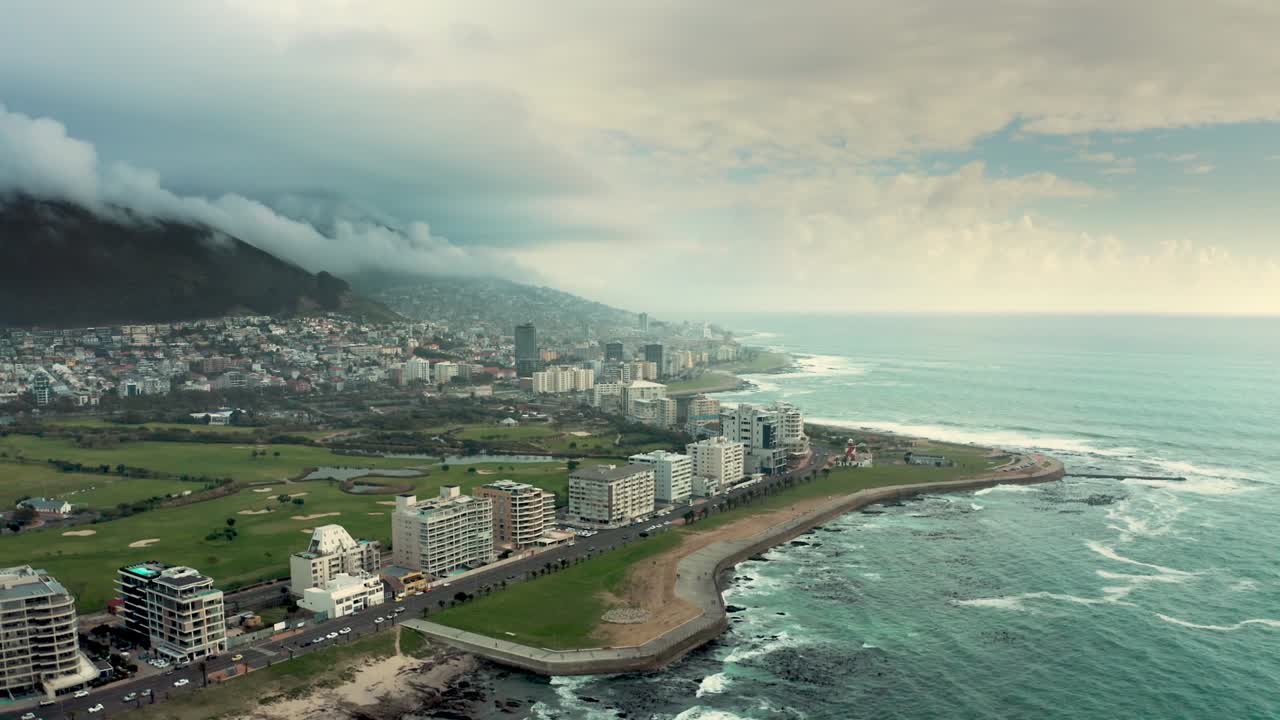 Aerial drone view captures city buildings lining coastline, with vast seascape stretching out against cloudy sky in Iceland, blending urban development with natural beauty of ocean