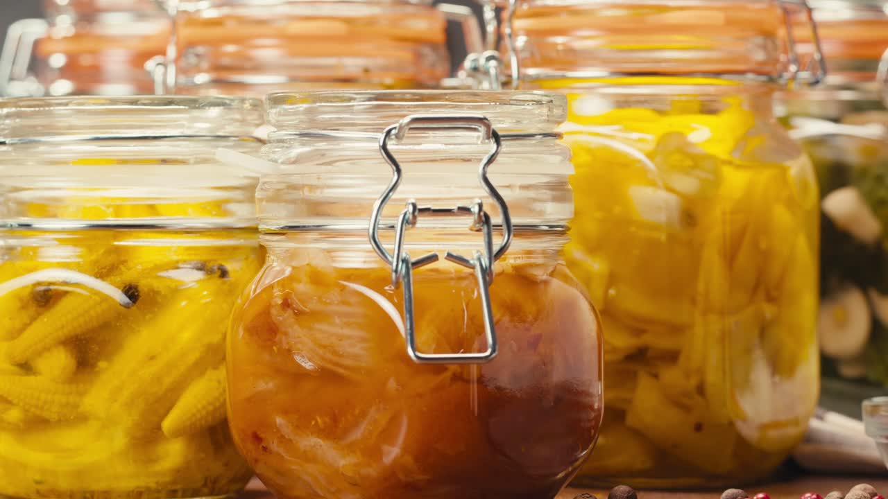Fermented food in glass cans on table close-up. Preservation of vegetables in glass jars. Fermentation preserved mini corns, kimchi, cucumbers, mushrooms with spices.
