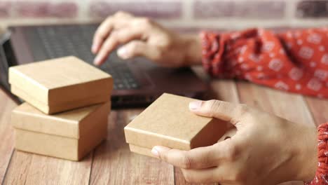 mujer sosteniendo una caja de regalos mientras trabaja en una computadora portátil
