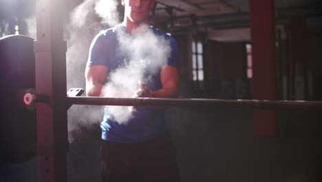 man chalking hands before lifting barbells in a gym