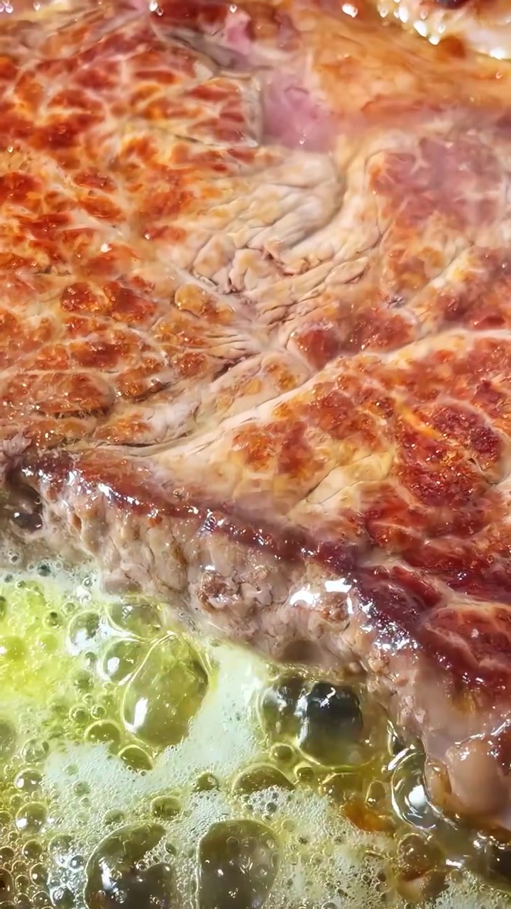 Un taglio di carne con crosta dorata sfrigola in olio d'oliva bollente su una piastra calda, catturando il momento clou del processo di rosolatura