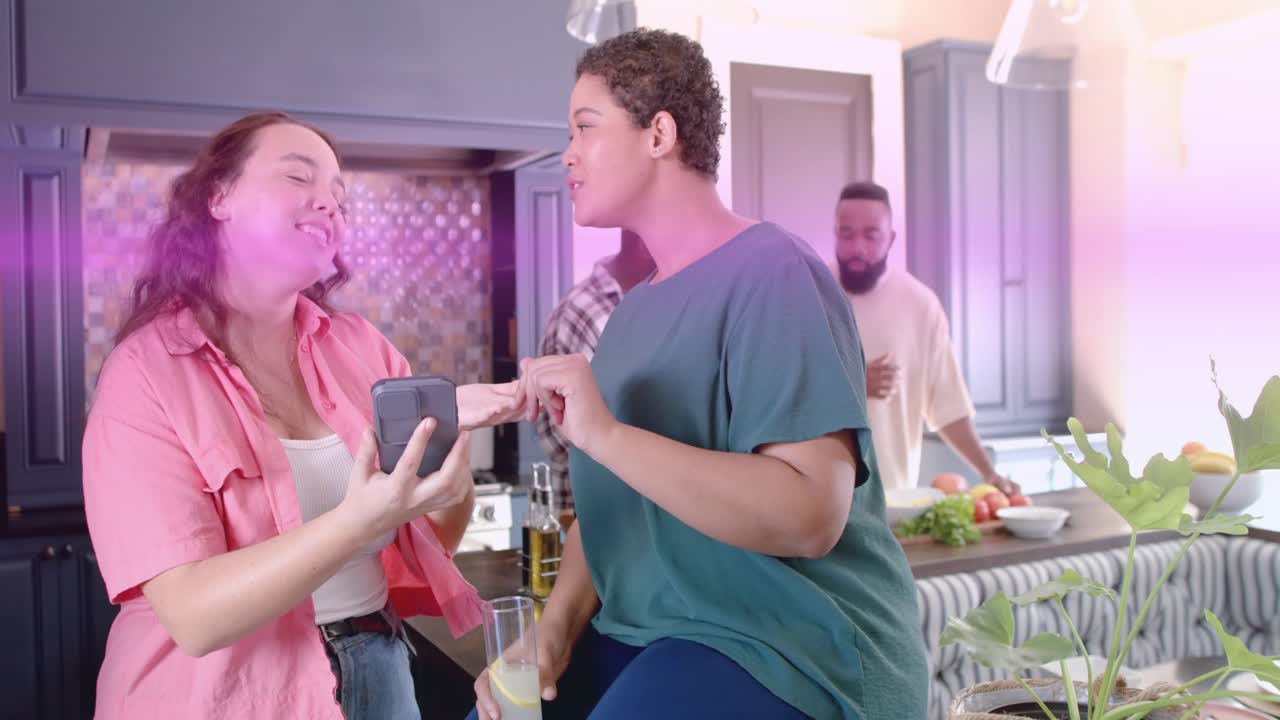 Two women tapping phone in kitchen singing to follow screen, pink lens flare sweeping, hiding scene
