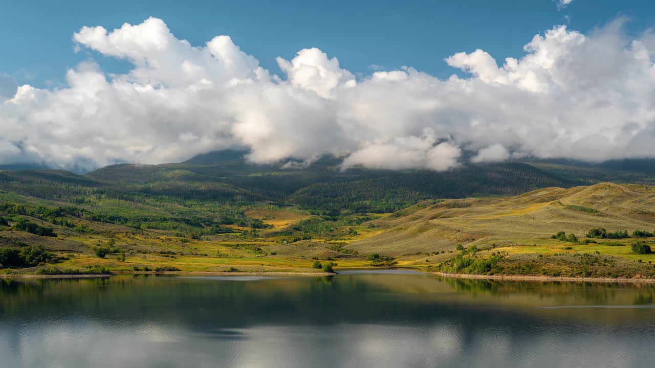 timelapse, nubes inversiones por encima del pico de la montaña, paisaje verde amarillo y lago en un día soleado