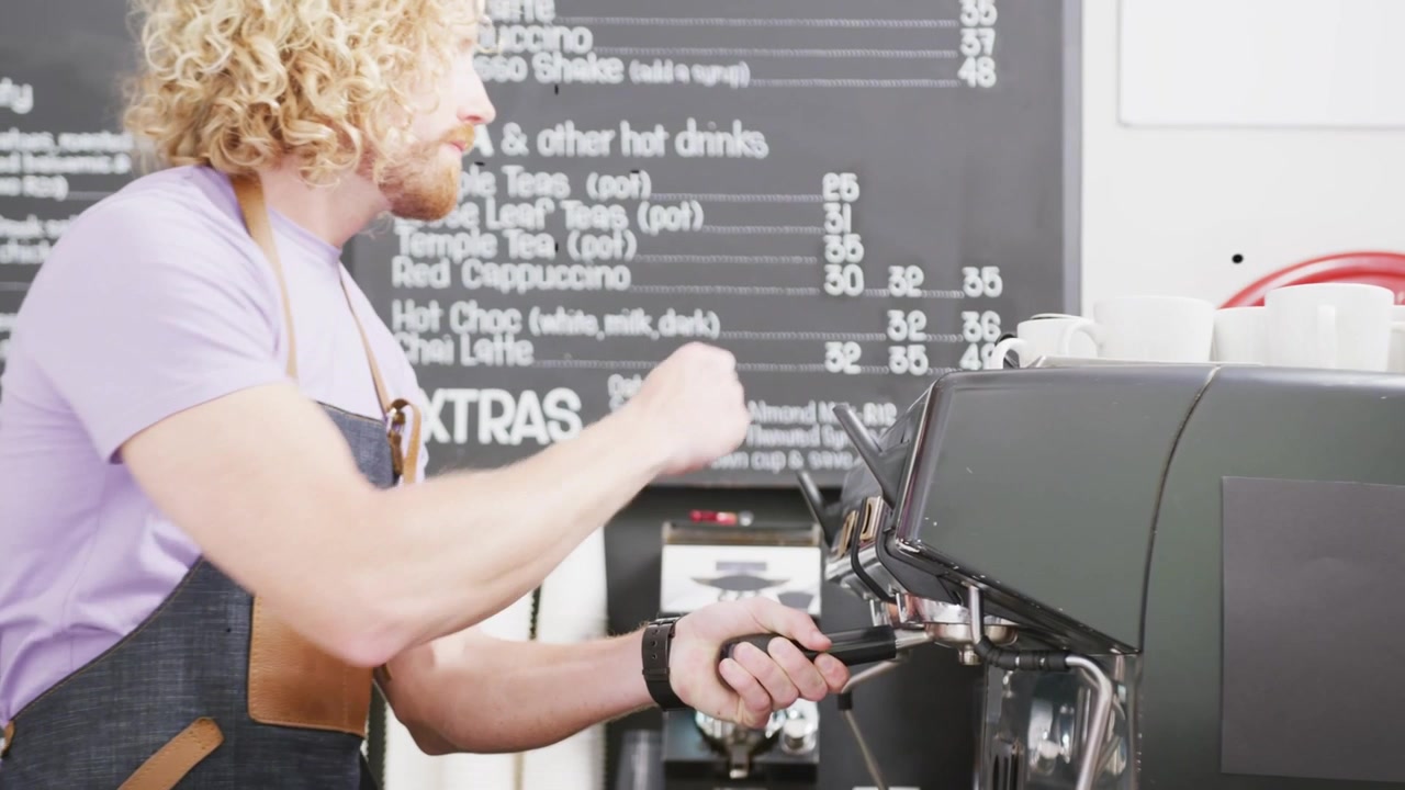 Barista uomo che allinea il portafiltro, posiziona la tazza ed eroga un espresso per un ordine, con sovrapposizioni che evidenziano il movimento