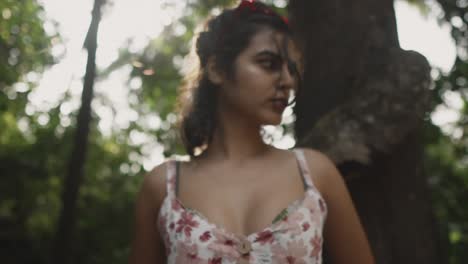 pan zoom out blurred portrait shot of a beautiful indian woman in the forest standing beside a tree