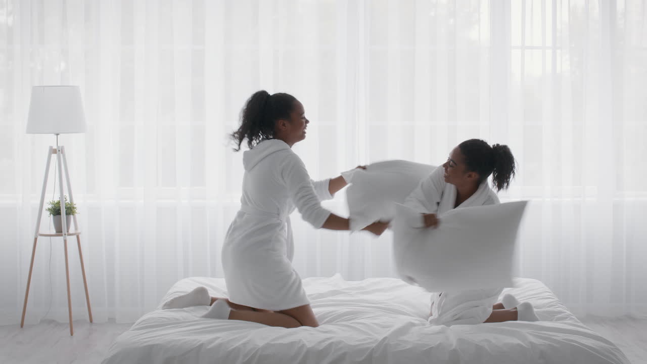 сестры весело сражаются по подушкам в спальне.